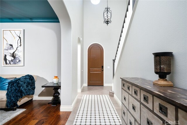 foyer featuring arched walkways, stairway, baseboards, and wood finished floors