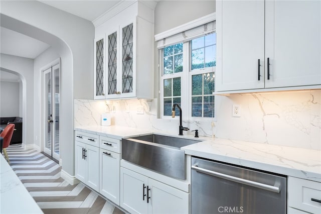 kitchen with a sink, glass insert cabinets, dishwasher, arched walkways, and light stone countertops