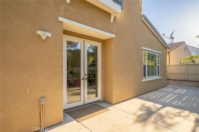 entrance to property featuring stucco siding, fence, a patio area, and french doors