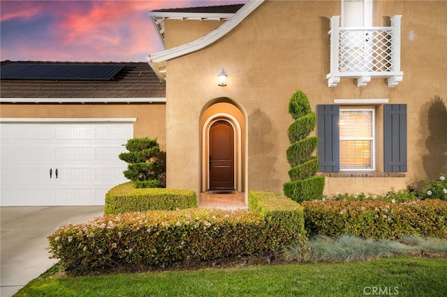 exterior entry at dusk featuring solar panels, concrete driveway, stucco siding, and a garage