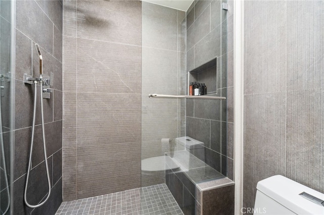bathroom with a tile shower, toilet, and tile patterned floors