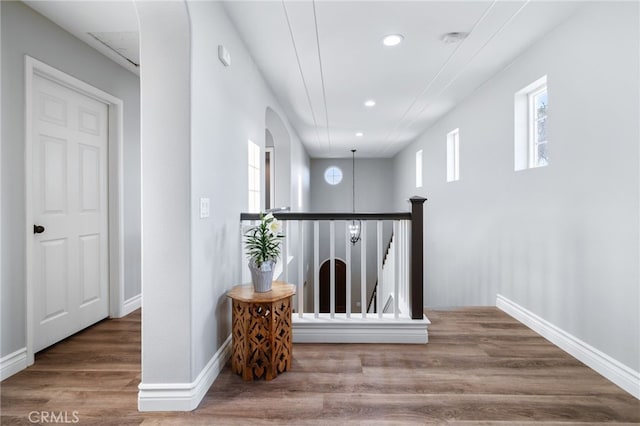 corridor featuring wood finished floors, arched walkways, recessed lighting, and a healthy amount of sunlight