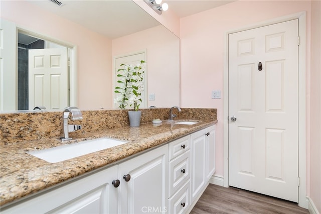 bathroom featuring visible vents, wood finished floors, a sink, and double vanity
