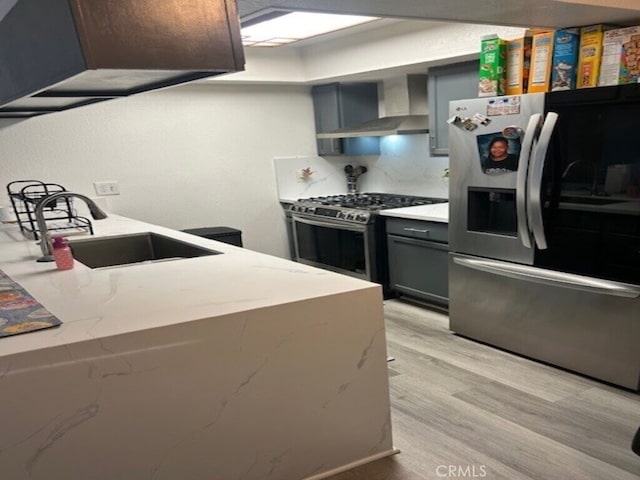 1508 Sunrise Rd, Barstow, CA 92311 - kitchen featuring appliances with stainless steel finishes, wall chimney range hood, a sink, light wood finished floors, and gray cabinetry