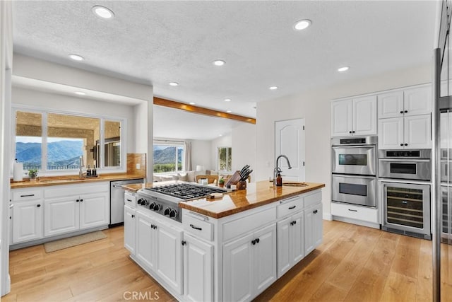 25174 Mulholland Hwy, Calabasas, CA 91302 - kitchen with stainless steel appliances, beverage cooler, a sink, a kitchen island with sink, and light wood-style floors