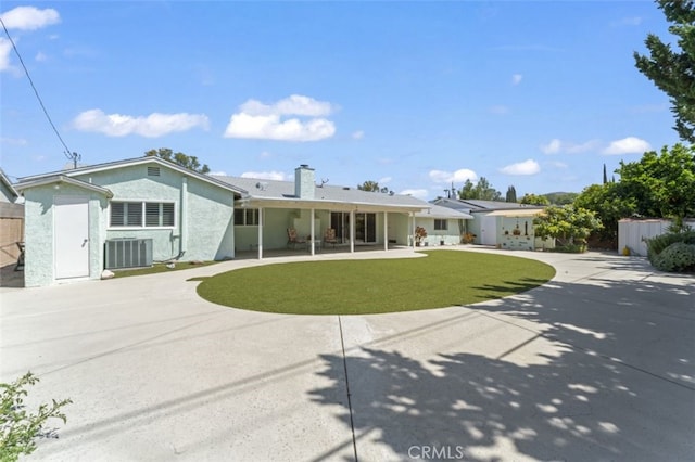 view of front of house featuring a patio area, central air condition unit, a front lawn, a chimney, and stucco siding