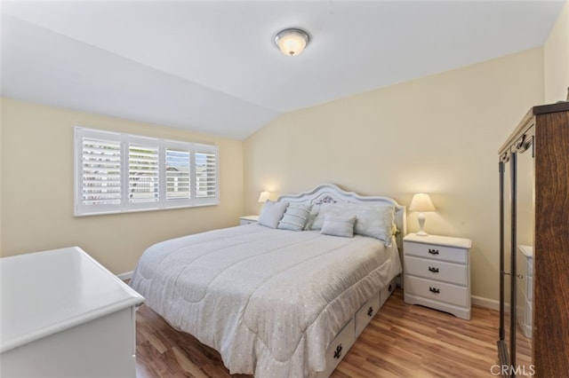 bedroom featuring light wood finished floors, baseboards, and lofted ceiling