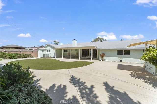 rear view of house featuring a chimney, fence, a lawn, a patio, and stucco siding