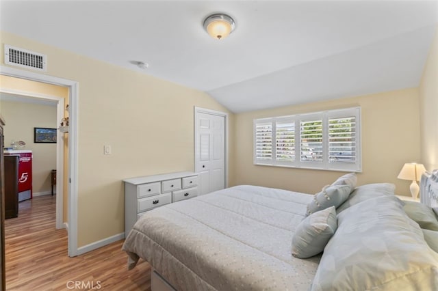 bedroom featuring baseboards, light wood-style flooring, visible vents, and vaulted ceiling