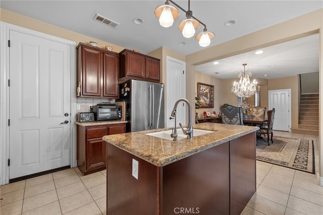 kitchen with a sink, a chandelier, light tile patterned flooring, visible vents, and freestanding refrigerator