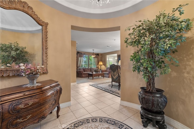 hall with light tile patterned floors, an inviting chandelier, and baseboards