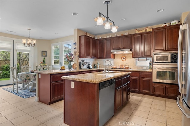 kitchen with a sink, an island with sink, light tile patterned floors, appliances with stainless steel finishes, and under cabinet range hood