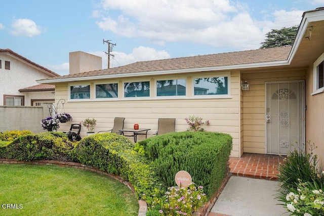 doorway to property featuring fence, a shingled roof, and a lawn