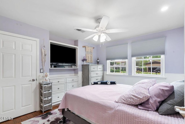 bedroom with visible vents, a ceiling fan, wood finished floors, and a wainscoted wall