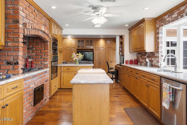 kitchen featuring ceiling fan, appliances with stainless steel finishes, a sink, light wood finished floors, and a kitchen island