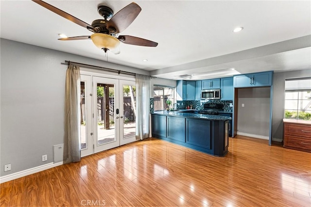 kitchen with dark countertops, french doors, stainless steel microwave, a peninsula, and blue cabinetry