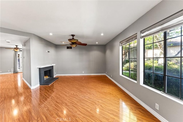unfurnished living room featuring light wood finished floors, a lit fireplace, baseboards, and ceiling fan