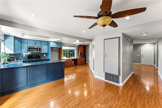 kitchen with a ceiling fan, light wood-type flooring, stainless steel microwave, a peninsula, and blue cabinetry