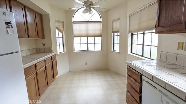 kitchen featuring tile counters, brown cabinets, light floors, a ceiling fan, and white appliances