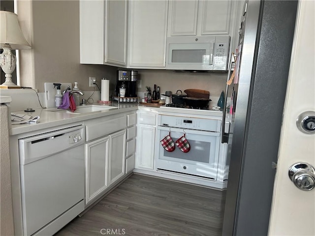 kitchen with a sink, wood finished floors, white appliances, light countertops, and white cabinetry