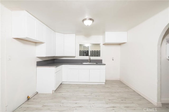 1181 W 4th St, Pomona, CA 91766 - kitchen featuring arched walkways, dark countertops, light wood-type flooring, and white cabinetry