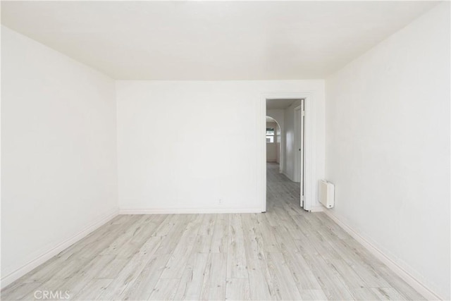 1181 W 4th St, Pomona, CA 91766 - unfurnished room featuring arched walkways, radiator, light wood-type flooring, and baseboards
