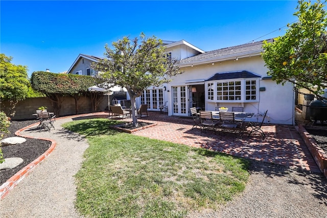rear view of property featuring a patio area, a yard, stucco siding, french doors, and fence