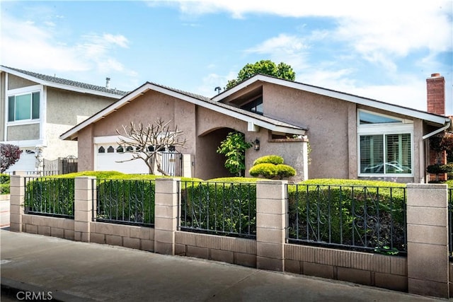mid-century modern home with a fenced front yard, an attached garage, a chimney, and stucco siding