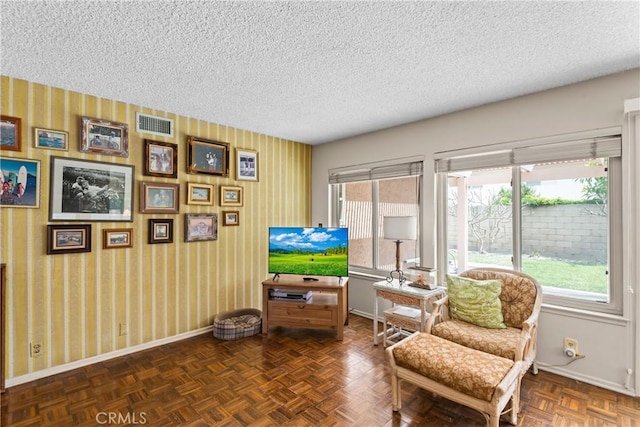 living area featuring baseboards, wallpapered walls, a textured ceiling, and visible vents