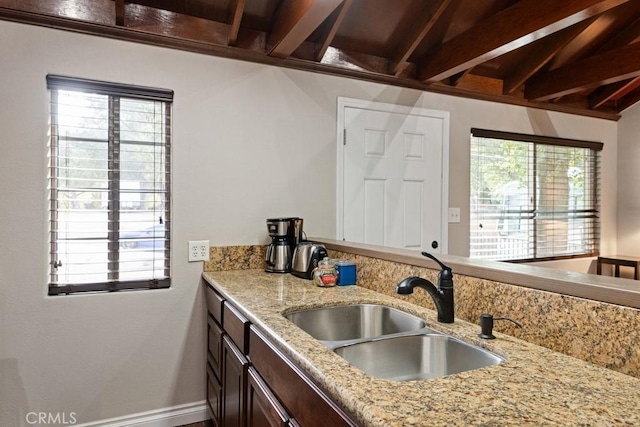 kitchen featuring dark brown cabinetry, beam ceiling, a sink, and a wealth of natural light