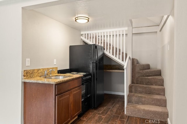kitchen with black range with gas cooktop, light stone counters, a sink, dark wood finished floors, and baseboards