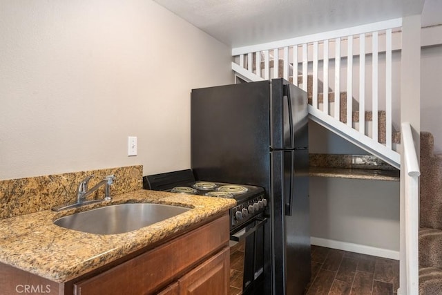 kitchen with dark wood finished floors, range with electric stovetop, a sink, light stone countertops, and brown cabinetry