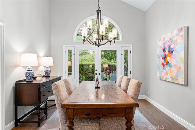 dining area with french doors, wood finished floors, high vaulted ceiling, baseboards, and a chandelier