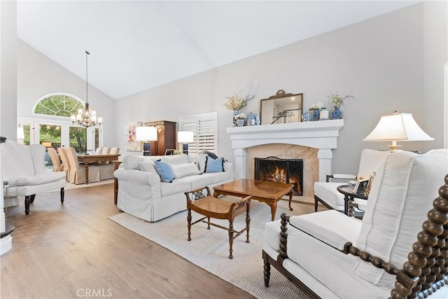 living room featuring high vaulted ceiling, a notable chandelier, light wood finished floors, and a high end fireplace