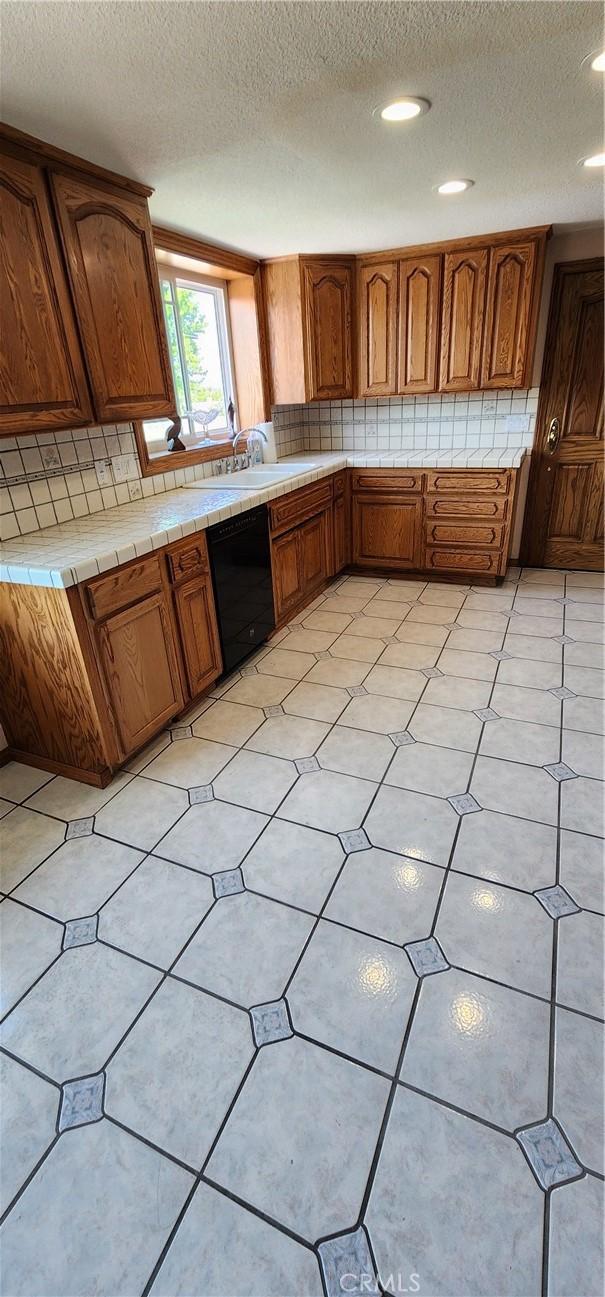kitchen with a textured ceiling, black dishwasher, and brown cabinets