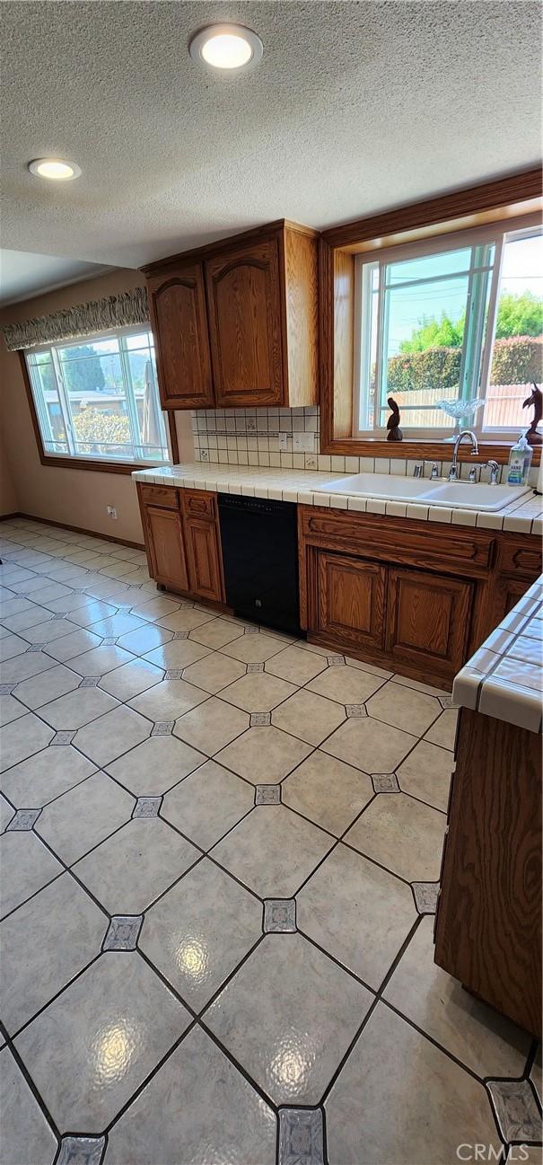 kitchen with black dishwasher, tile counters, a textured ceiling, and brown cabinets