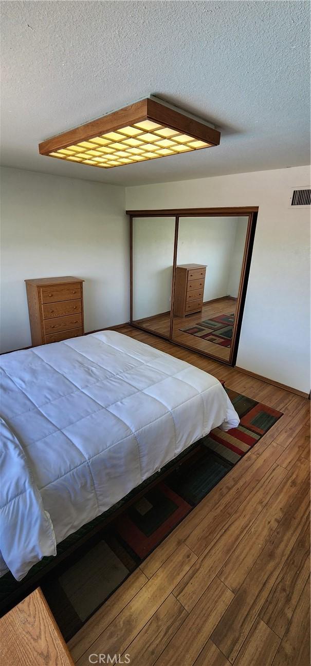 bedroom featuring wood-type flooring, a closet, a textured ceiling, and visible vents