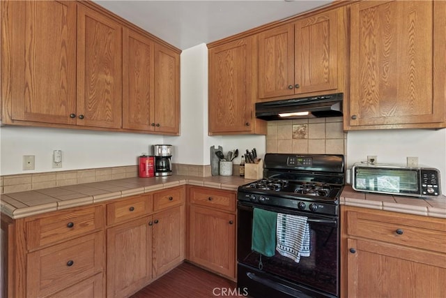 29278 Pine Dr, Cedar Glen, CA 92321 - kitchen featuring black range with gas stovetop, under cabinet range hood, tile counters, backsplash, and brown cabinetry