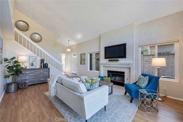 living area featuring a fireplace, high vaulted ceiling, stairs, baseboards, and wood finished floors