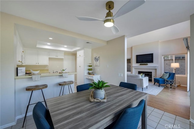 dining room featuring ceiling fan, visible vents, a fireplace, a tray ceiling, and light tile patterned flooring