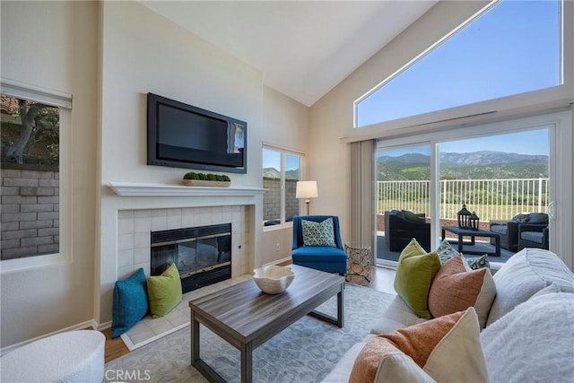 living room with a tiled fireplace, high vaulted ceiling, baseboards, and wood finished floors