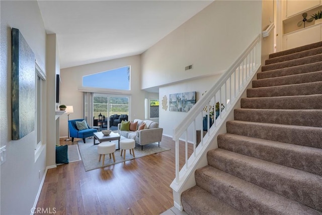 stairs with baseboards, a towering ceiling, wood finished floors, and visible vents