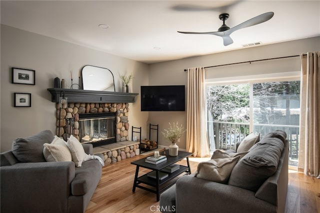 living area featuring wood finished floors, visible vents, a ceiling fan, and a stone fireplace
