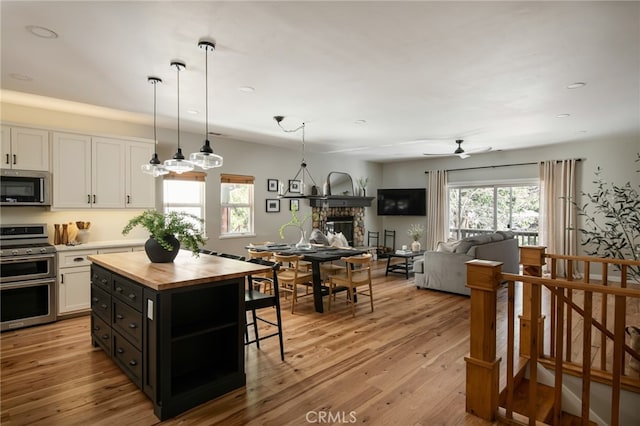 kitchen featuring white cabinets, wood counters, a stone fireplace, a breakfast bar, and appliances with stainless steel finishes
