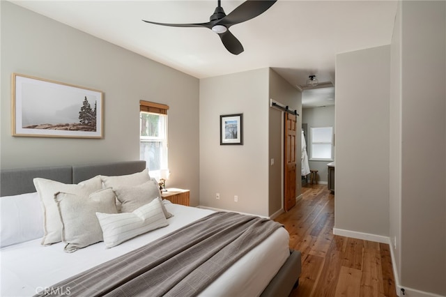 bedroom featuring a barn door, baseboards, a ceiling fan, and light wood-type flooring