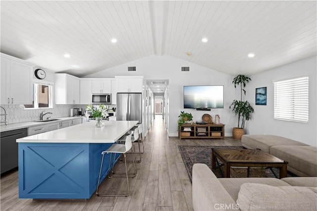 kitchen with vaulted ceiling with beams, open floor plan, stainless steel appliances, and a sink