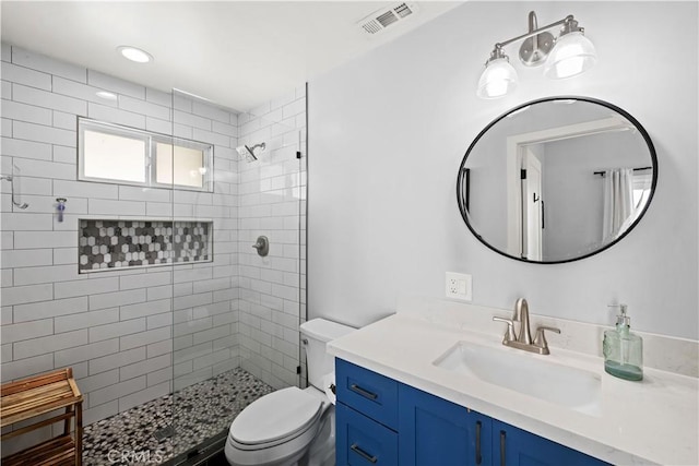 full bathroom with a tile shower, visible vents, toilet, and vanity
