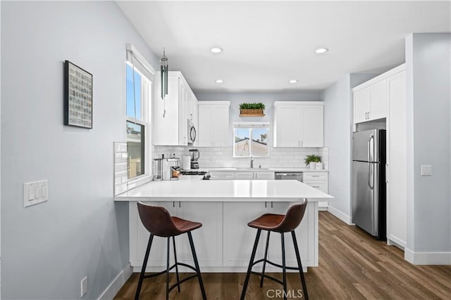 kitchen featuring tasteful backsplash, a sink, baseboards, a peninsula, and appliances with stainless steel finishes