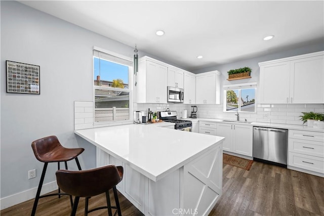 kitchen featuring a kitchen breakfast bar, backsplash, a sink, a peninsula, and appliances with stainless steel finishes
