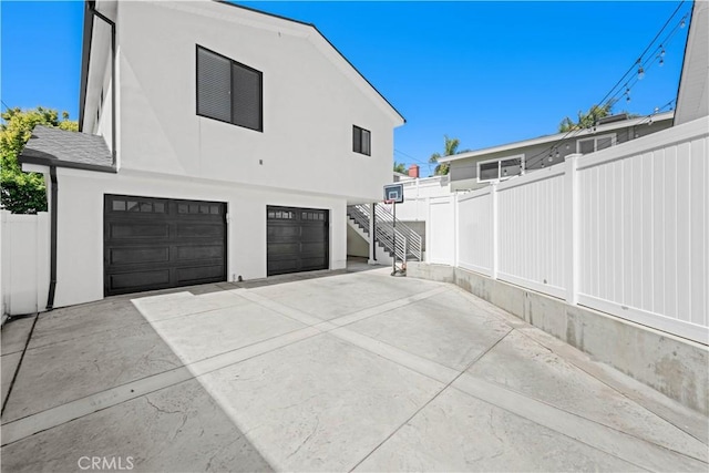 view of side of home featuring concrete driveway, an attached garage, fence, and stairway